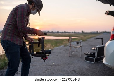 Young cinematographer using gimbal stabilizer shooting video footage for content creator of him on the location outdoor.