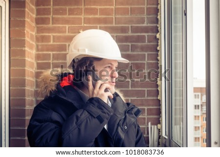 Young civil engineer is having trouble over the phone against brick background. Soft focus, toned.