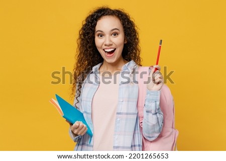 Young clever black teen girl student she wear casual clothes backpack bag write in notebook hold finger up great new idea isolated on plain yellow background. High school university college concept