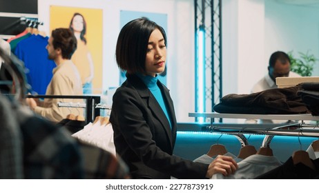 Young client shopping in fashionable boutique shop, looking at formal wear on hangers and racks. Woman buying trendy store merchandise from shopping mall, commercial activity. - Shutterstock ID 2277873919
