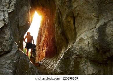 Young climber standing with rope and looking at rocky wall in a cave