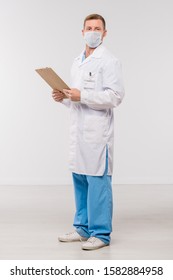 Young Clinician In Whitecoat And Protective Mask Holding Clipboard With Medical Document In Isolation