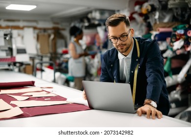 Young clothing designer using computer while working at textile workshop.
