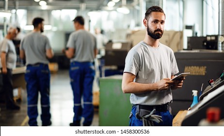 Young CNC machine operator using touchpad while working in a factory and looking at camera.  