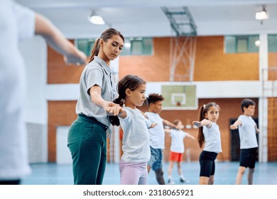 Young coach assisting her elementary students during physical activity class at school gym. - Powered by Shutterstock