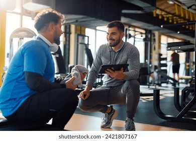 Young coach communicating with mature man while using digital tablet during sports training in health club.  - Powered by Shutterstock