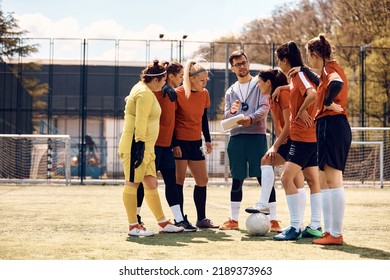 Young coach giving instructions to female soccer team while planning strategy for the match on football pitch. - Powered by Shutterstock