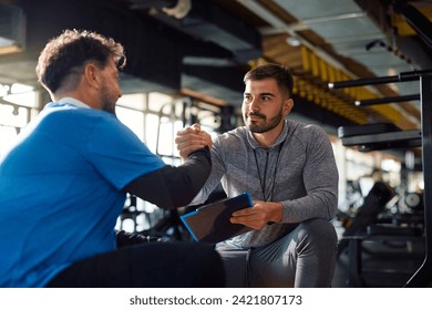 Young coach giving a manly handshake to mature man after successful sports training in a gym. - Powered by Shutterstock