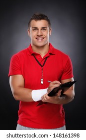 Young Coach. Portrait Of Cheerful Young Coach Holding A Clipboard And Whistle.