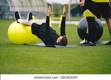 Young Coach Showing To Junior Players How To Exercise Properly On Training Mat And Training Yoga Ball. High Performance Sports Training For Youth Athletes