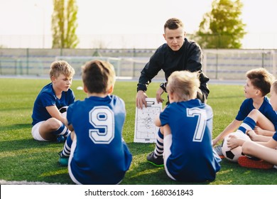 Young Coach Teaching Kids On Football Field. Football Coach Coaching Children. Soccer Football Training Session For Children. Football Tactic Education. Coach Explains A Game Strategy Using Board