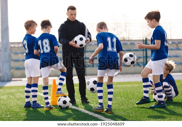 Young coach teaching kids on football field. Trainer\
explains to schoolboys training rules. Football coach coaching\
children. Soccer football training session for children. Football\
tactic education. 