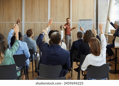 Young colleagues raising hands to ask questions during business meeting in office. Diverse business people voting at the conference in meeting room listening their young male speaker. - Powered by Shutterstock