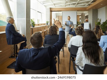 Young colleagues raising hands to ask questions during business meeting sitting back in office. Diverse business people voting at the conference in meeting room listening their speaker. - Powered by Shutterstock