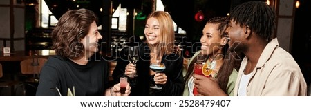 Young colleagues share laughter while toasting with colorful drinks at a corporate gathering.
