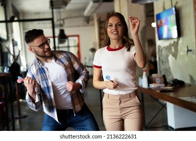 Young colleagues taking break after work. Happy young businessman and businesswoman playing darts in the office.	 - Shutterstock ID 2136222631