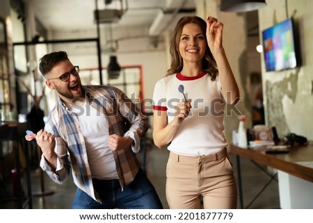 Young colleagues taking break after work. Happy young businessman and businesswoman playing darts in the office.	