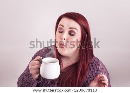 Young college aged female woman blowing on a steaming cup of hot caffeinated coffee