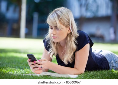 Young College Girl Using Cell Phone While Lying On Grass