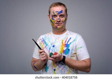 Young comedy, funny guy (architect, designer, web designer) with brushes in their hands smeared in colored paint posing and laughing in the studio in a white sports shirt