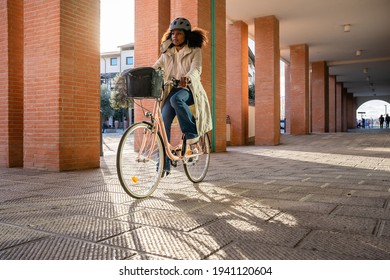 Young Commuter Woman In City In Sustainable Way Wearing Bike Helmet With Protective Face Mask Against Coronavirus Covid-19 Pandemic Rides Her Bicycle On Way Home To Work - Safety And Commuting Concept