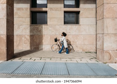 Young Commuter Woman In City In Sustainable Way With Bike Helmet Wearing Protective Face Mask Against Coronavirus Covid-19 Pandemic Leads By Hand Bicycle Way Home To Work Safety And Commuting Concept