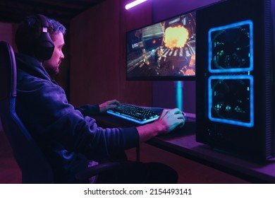 Young concentrated cyber sportsman playing in FPS video game on his personal computer in dark neon room. Pro gamer participating in online esport competition. Cyber games championship event concept