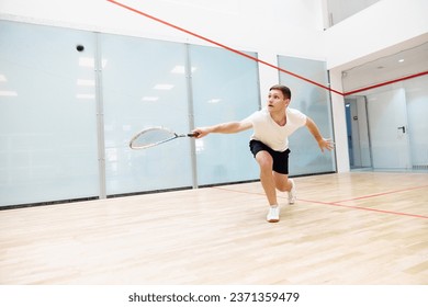 Young concentrated man in sportswear playing, training squash on squash court. Leisure healthy time. Concept of sport, hobby, healthy and active lifestyle, game, gym, ad