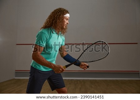 Young concentrated squash player practicing serve while exercising game at gym