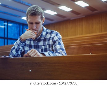 Young Concentrated Thinking Student Sitting In The Empty Big Lecture Hall On Exam