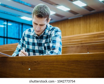 Young Concentrated Thinking Student Sitting In The Empty Big Lecture Hall On Exam