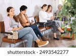 Young concentrated woman in casual clothes sits on chair in waiting room waiting for her turn