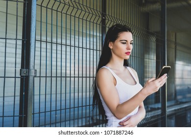 A young concentrated woman reads a message on the phone. The girl is holding the phone in hand. Female in a white T-shirt with sunglasses looks at the phone in consternation outside.