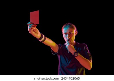 Young concentrated woman, soccer referee blowing a whistle and showing red card as dismissal symbol on black studio background in neon. Concept of sport, competition, match, profession, football game - Powered by Shutterstock