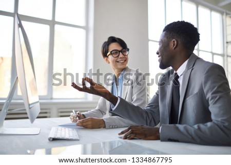 Young confident analyst or broker explaining his colleague rate change tendencies in front of computer monitor