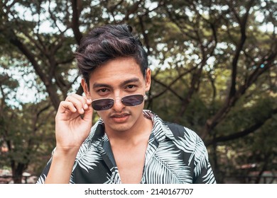 A Young Confident Asian Man With A Flirty Look. Checking Out Someone In The Park. Lowering His Sunglasses Down.