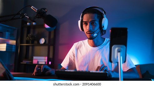 Young confident Asian man playing online computer video game, colorful lighting broadcast streaming live at home. Gamer lifestyle, E-Sport online gaming technology concept - Shutterstock ID 2091406600