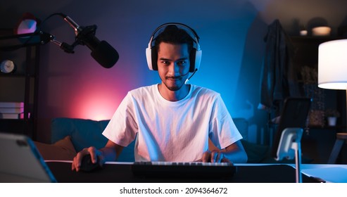 Young confident Asian man playing online computer video game, colorful lighting broadcast streaming live at home. Gamer lifestyle, E-Sport online gaming technology concept - Shutterstock ID 2094364672