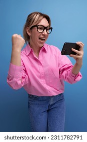 young confident blond woman with ponytail and glasses dressed in a trendy pink shirt for the office watching video - Shutterstock ID 2311782791