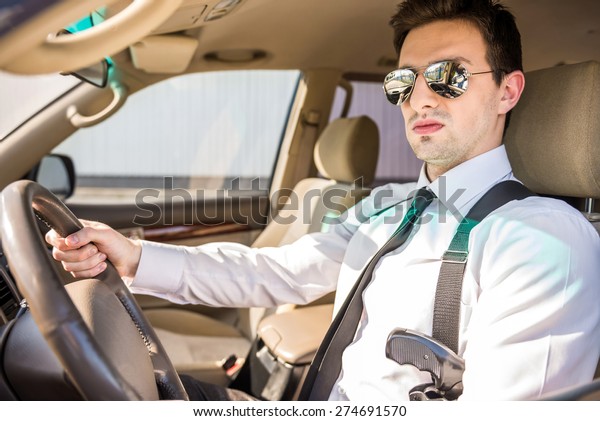 Young confident  businessman  in\
sunglasses with gun sitting in his luxurious\
car.