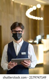 Young Confident Businessman Or Worker Of Modern Hotel In Uniform, Eyeglasses And Protective Face Mask Standing In Front Of Camera