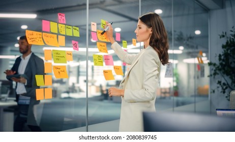 Young Confident Businesswoman Creating Project Plan on Office Wall with Paper Notes. Stylish Beautiful Manager Working on Business, Financial and Marketing Projects. Specialist in Diverse Team. - Powered by Shutterstock