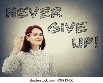 Young  confident businesswoman  holding pencil pointed to face  drawing text over head  Never give up  positive thinking concept isolated grey wall background 