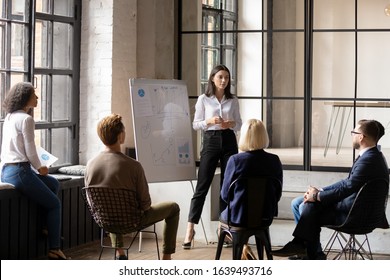 Young confident ceo make forecast financial report on flip chart for diverse staff, group of workmates listen woman business trainer take part at educational meeting in modern office coaching concept - Shutterstock ID 1639493716