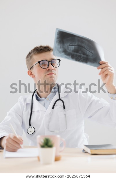 a young and confident doctor in the medical office\
looks at the documents and radiographs of the patient and makes a\
conclusion about the disease. the doctor sees the patient in his\
office, modern