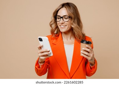 Young confident employee business woman corporate lawyer 30s wear classic formal orange suit glasses work in office hold use mobile cell phone drink coffee isolated on plain beige background studio - Powered by Shutterstock