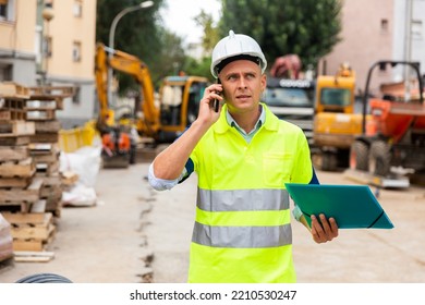 Young confident engineer working at a construction site is talking on a mobile phone, discussing important issues - Shutterstock ID 2210530247