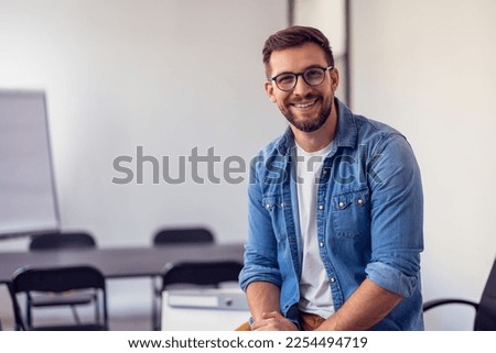 Young confident entrepreneur sitting in modern office smiling and looking at camera.