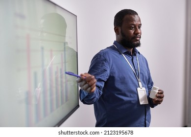 Young Confident Expert With Bottle Of Vitamins Making Presentation Of Financial Charts And Sales Rate Of New Medicaments