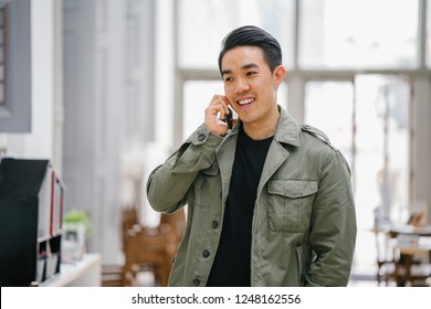 A young, confident and good-looking Chinese Asian man is speaking on his smartphone. He is comfortably dressed in casual clothing and is smiling.   - Powered by Shutterstock